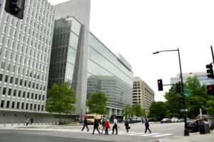 People crossing a street near modern glass office buildings.